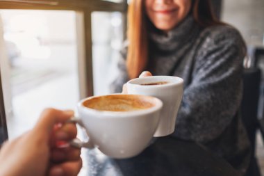 Closeup image of a woman and a man clinking coffee mugs in cafe
