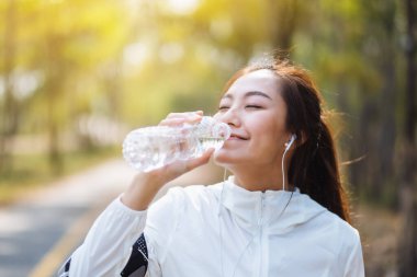 Şehir parkında koştuktan sonra şişeden su içen Asyalı bir koşucunun yakın plan görüntüsü.