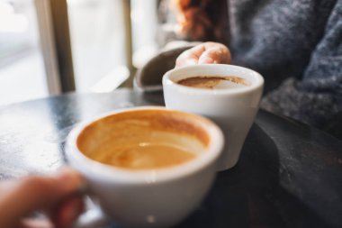 Closeup image of a woman and a man clinking coffee mugs in cafe