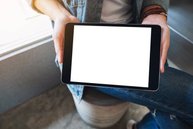 Kafedeki boş beyaz ekranlı siyah tableti tutan ve gösteren bir kadının görüntüsü