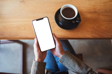 Kafede otururken elinde boş masaüstü ekranıyla siyah cep telefonu tutan bir kadının üst görünüm görüntüsü