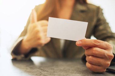 Bir iş kadını boş bir kartviziti tutarken iyi bir işaret göstermek için parmağını kaldırıyor.