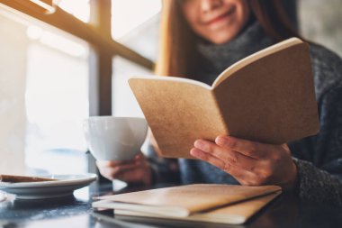 Closeup image of a beautiful woman reading a book while drinking coffee in the morning