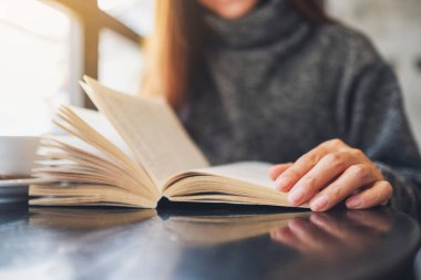 Closeup image of a beautiful woman holding and reading a book with coffee cup on the table