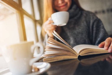 Closeup image of a beautiful woman reading a book while drinking coffee in the morning