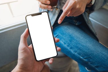 Birinin elinde boş siyah masaüstü ekranı olan beyaz bir cep telefonunu gösteren bir kadının görüntüsü.