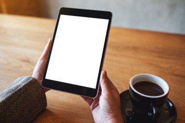 Siyah tabletli, beyaz ekranlı ve ahşap masada kahve fincanı olan bir kadının görüntüsü. 