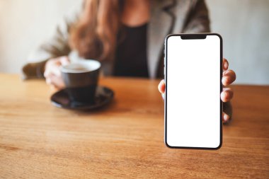 Kafede kahve içerken siyah cep telefonunu beyaz ekran ile tutan ve gösteren bir iş kadını görüntüsü.