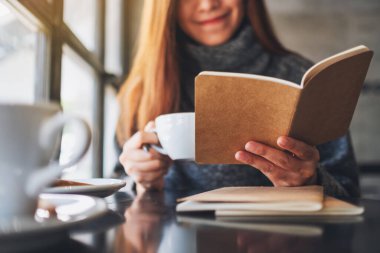 Kafede kahve içerken kitap okuyan Asyalı güzel bir kadının yakın plan görüntüsü. 