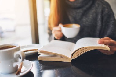 Closeup image of a woman reading a book while drinking coffee in cafe 