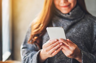 Kafe 'de elinde kahve fincanı olan ve cep telefonu kullanan bir kadının yakın plan fotoğrafı.