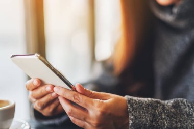 Closeup image of a woman holding and using mobile phone with coffee cup on the table in cafe