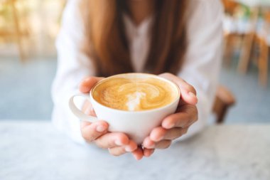 Elinde bir fincan sıcak kahve tutan ve gösteren bir kadının yakın plan görüntüsü.