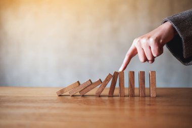 Bir parmağın yakın plan görüntüsü iş çözümü kavramı için tahta domino taşlarını engellemeye çalışıyor. 