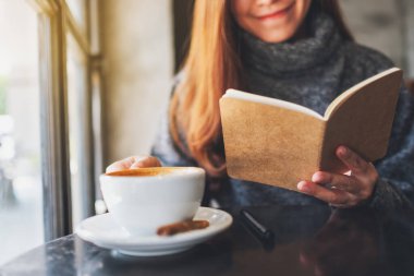 Closeup image of a beautiful woman reading a book while drinking coffee in the morning