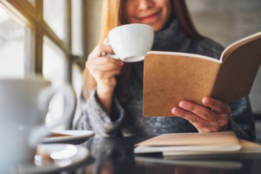 Closeup image of a beautiful woman reading a book while drinking coffee in the morning