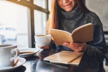 Closeup image of a beautiful woman reading a book while drinking coffee in the morning