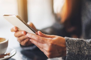 Closeup image of a woman holding and using mobile phone with coffee cup on the table in cafe