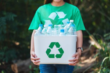 Çöp toplayan ve elinde plastik şişelerle geri dönüşüm kutusunu tutan bir kadın.
