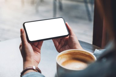 Masasında kahve fincanı olan, elinde siyah bir cep telefonu olan bir kadının görüntüsü.