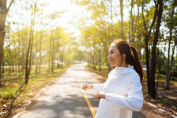 Genç Asyalı bir kadın şehir parkında koşmadan önce kollarını esnetiyor. 
