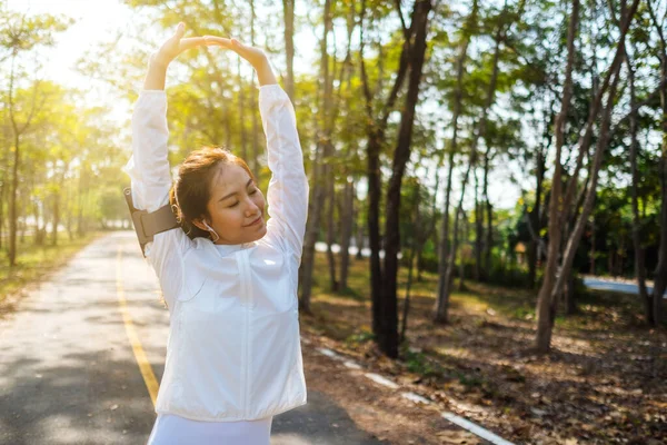 Genç Asyalı bir kadın şehir parkında koşmadan önce kollarını esnetiyor. 