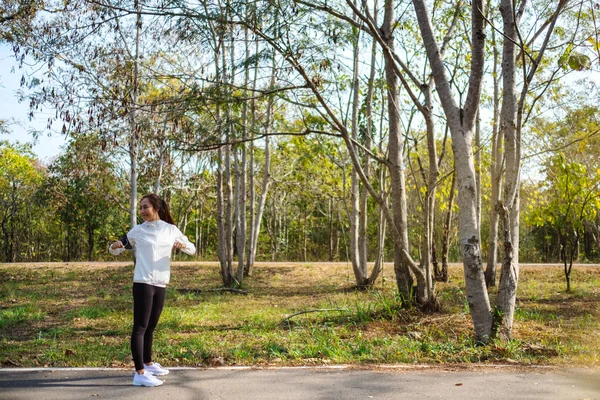 Genç Asyalı bir kadın şehir parkında koşmadan önce kollarını esnetiyor. 