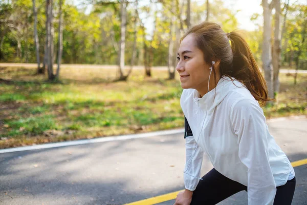 Yorgun Asyalı bayan koşucu sabah şehir parkında koştuktan sonra dinleniyor.