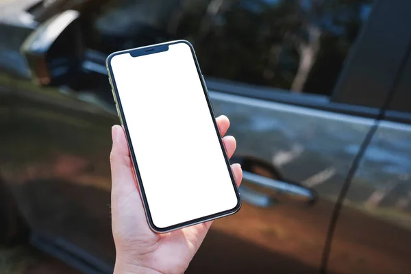 stock image Mockup image of a woman holding and using mobile phone with blank screen with a car in background