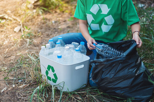 A woman picking up garbage plastic bottles into a box and bag for recycling concept