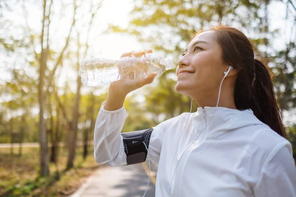 Şehir parkında koştuktan sonra şişeden su içen Asyalı bir koşucunun yakın plan görüntüsü.