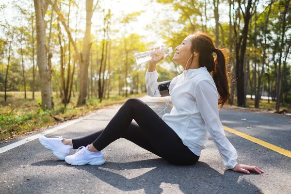 Şehir parkında koştuktan sonra şişeden su içen Asyalı bir koşucunun yakın plan görüntüsü.