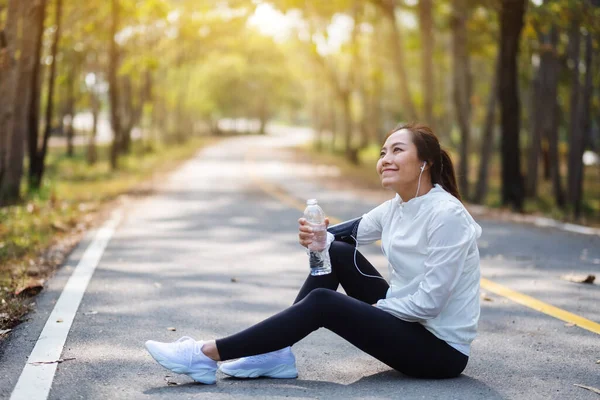Şehir parkında koştuktan sonra elinde su şişesi tutan Asyalı bir sporcunun yakın plan fotoğrafı.