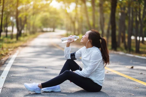 Şehir parkında koştuktan sonra şişeden su içen Asyalı bir koşucunun yakın plan görüntüsü.