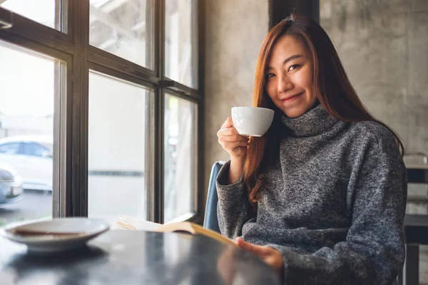 Kafede kahve içerken kitap okuyan Asyalı güzel bir kadının yakın plan görüntüsü. 