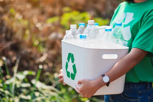 A woman collecting garbage and holding a recycle bin with plastic bottles in the outdoors