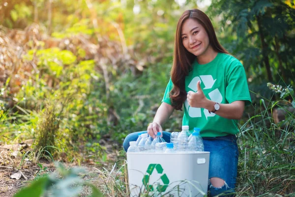 Güzel bir Asyalı kadın, dışarıda çöp kutusuna plastik şişe toplarken el işareti yapıyor.