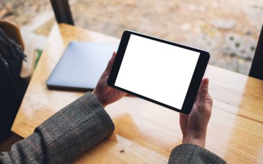 Siyah tabletli, beyaz ekranlı ve tahta masadaki laptoplu bir kadının görüntüsü. 