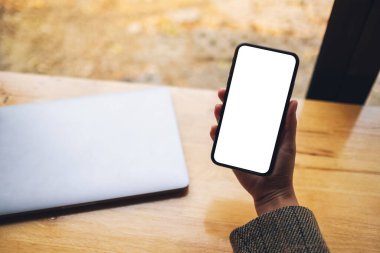 Masasında dizüstü bilgisayarı olan, boş beyaz masaüstü ekran cep telefonu tutan bir kadının en üstteki görüntüsü 