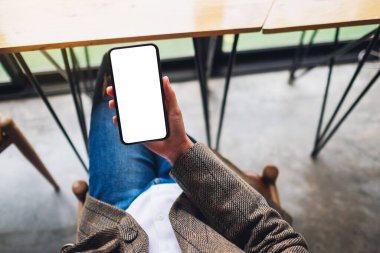 Ofiste otururken elinde boş beyaz ekranla cep telefonu tutan bir kadının üst görünüm görüntüsü