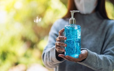 Koruyucu maske takan ve Sağlık ve Covid-19 konsepti için bir şişe alkol jeli dezenfektanı gösteren bir kadının yakın plan görüntüsü.