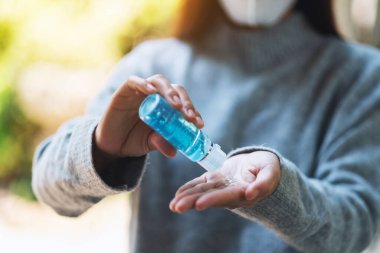 Korumalı maske takan Asyalı bir kadının sağlık ve Covid-19 konsepti için temiz ellere alkol jeli sürerken yakın plan görüntüsü.