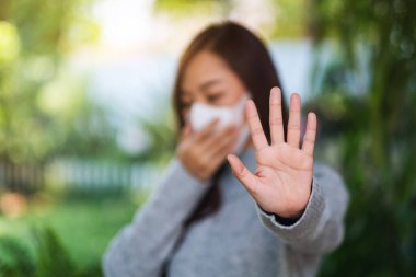 Korumacı yüz maskesi takan Asyalı bir kadının yakın plan görüntüsü Covid-19 'un yayılmasını önlemek için dur işareti yapıyor.  