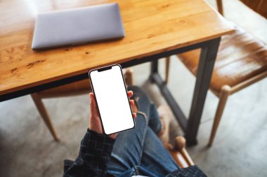 Masasında dizüstü bilgisayarı olan, boş beyaz masaüstü ekran cep telefonu tutan bir kadının en üstteki görüntüsü 