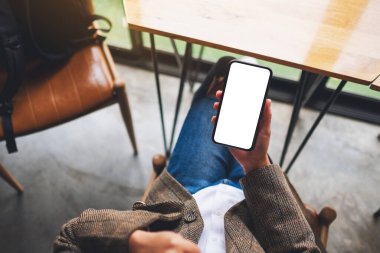 Ofiste otururken elinde boş beyaz ekranla cep telefonu tutan bir kadının üst görünüm görüntüsü