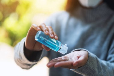 Closeup image of a woman wearing a protective mask and applying alcohol gel to clean hands for Healthcare and Covid-19 or 2020 virus concept