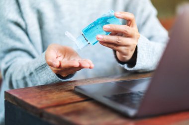 Sağlık ve Covid-19 veya 2020 virüs konsepti için evde dizüstü bilgisayar üzerinde çalışırken alkol jeli kullanan ve uygulayan bir kadının yakın plan görüntüsü