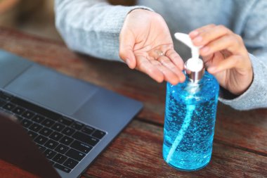 Sağlık ve Covid-19 veya 2020 virüs konsepti için evde dizüstü bilgisayar üzerinde çalışırken alkol jeli kullanan ve uygulayan bir kadının yakın plan görüntüsü