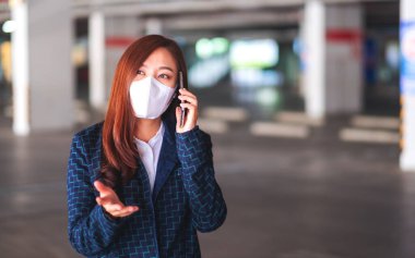 Korumacı yüz maskesi takan Asyalı bir kadının sağlık ve Covid-19 konsepti için cep telefonuyla konuşma ve kullanma görüntüsü.