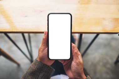 Ofiste otururken elinde boş beyaz ekranla cep telefonu tutan bir kadının üst görünüm görüntüsü